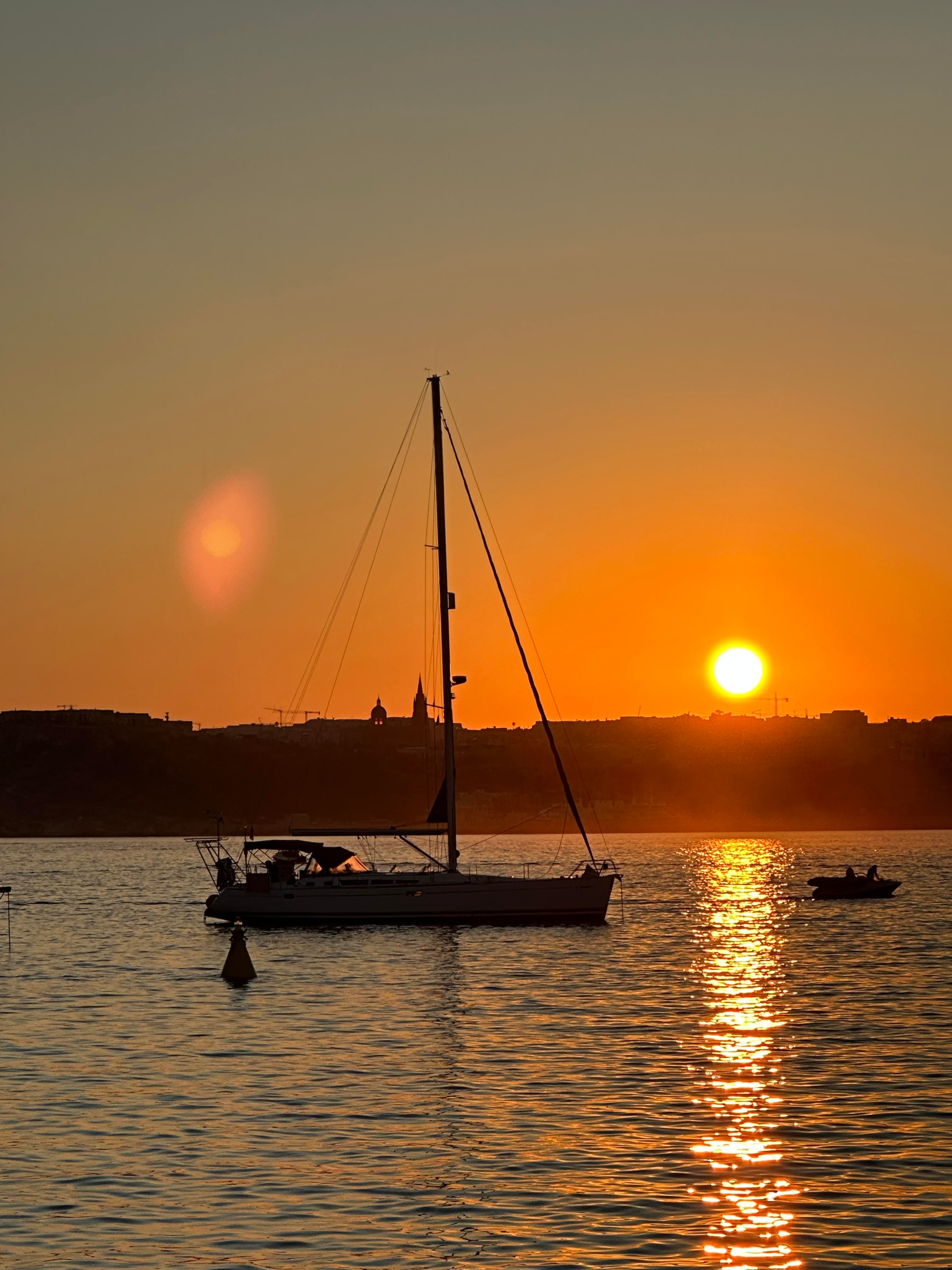 Sunset over Comino’s Blue Lagoon, Malta, with golden light reflecting on turquoise waters and boats anchored nearby.