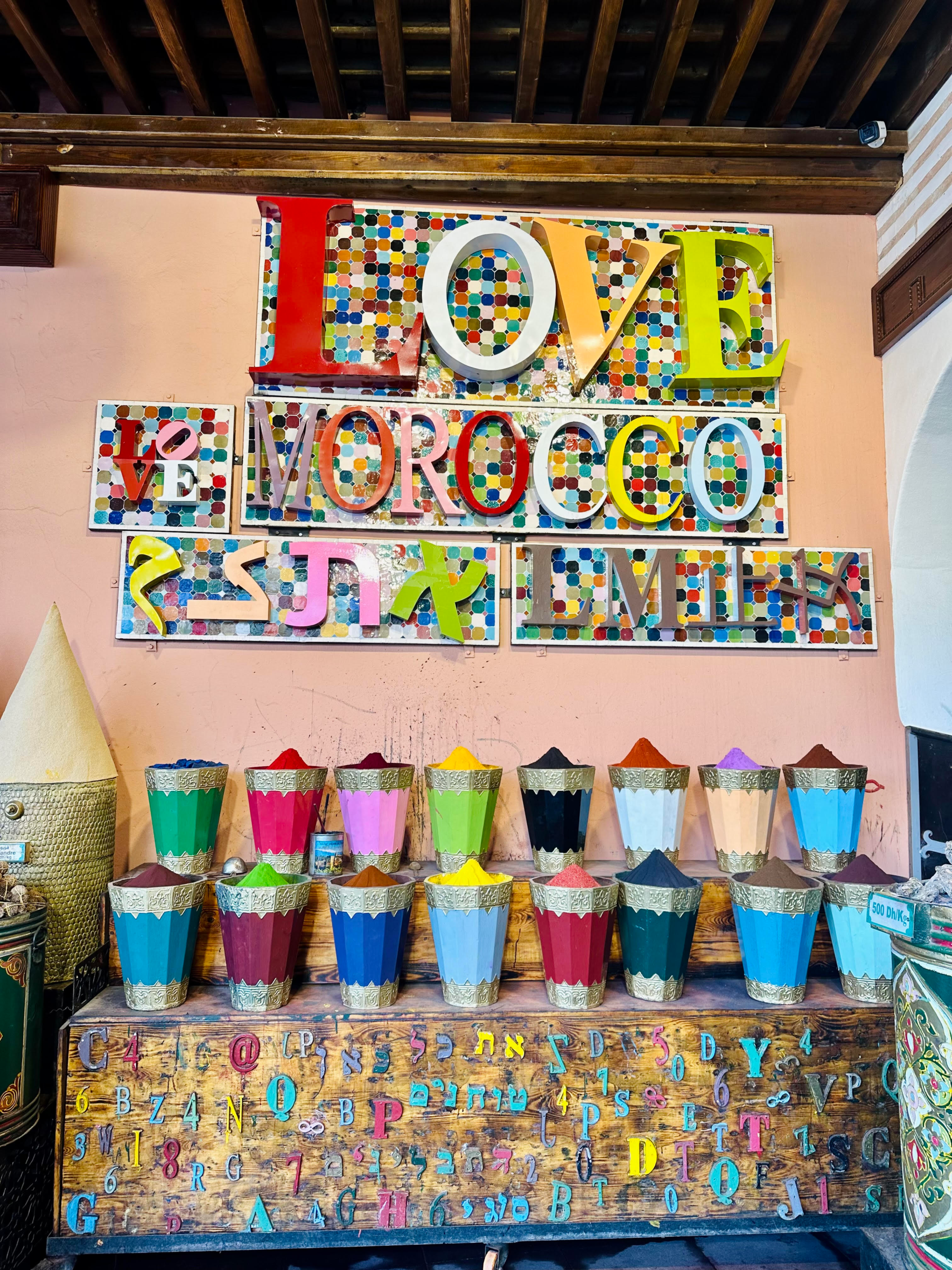 I Love Morocco” sign above colorful spice cones in the Marrakech medina souks.