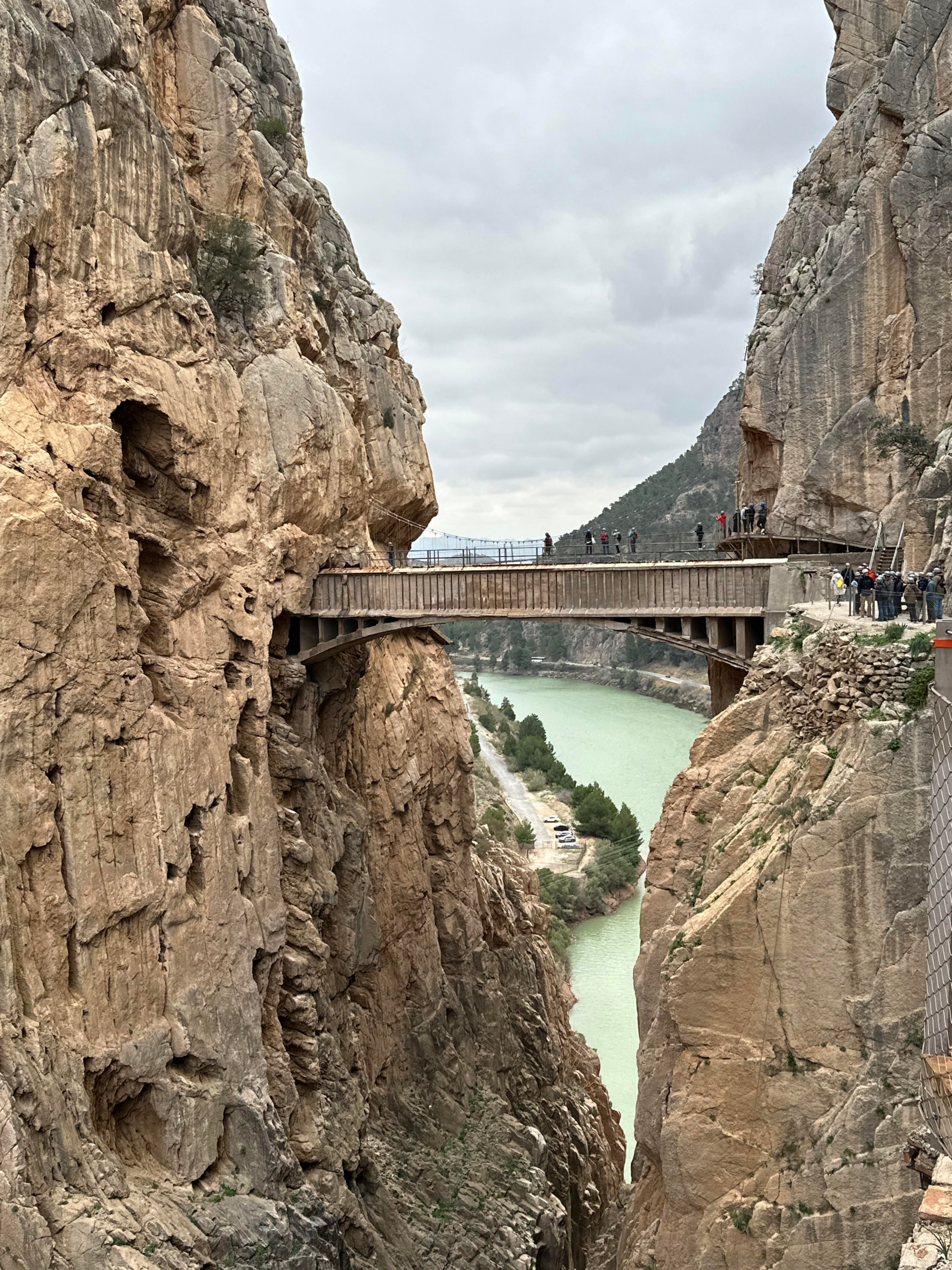 Suspended bridge on the Caminito del Rey with the river flowing below and towering cliffs on both sides, showcasing the dramatic gorge scenery.